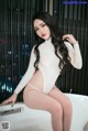 A woman in a white bodysuit sitting on a bathtub.