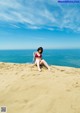 A woman in a red bikini sitting on a sandy beach.