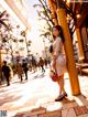 A woman in a white dress is standing on a sidewalk.