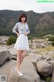 A woman standing on a rock in a white dress.