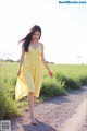 A woman in a yellow dress walking down a dirt road.