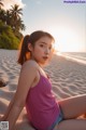 A woman in a pink tank top sitting on a beach.