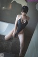 A woman in a black bathing suit sitting on a bathtub.