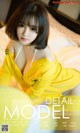 A woman in a yellow dress sitting on a bed.