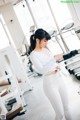 A woman in a white top and white leggings in a gym.