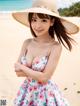 A woman in a dress and hat on the beach.