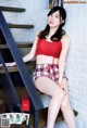 A woman in a red top and plaid shorts sitting on a staircase.