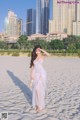 A woman in a white dress standing on a sandy beach.