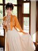 A woman in an orange kimono posing in front of a window.