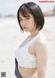 A woman in a white tank top standing on a beach.