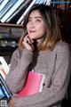 A woman sitting in front of a book shelf holding a book.